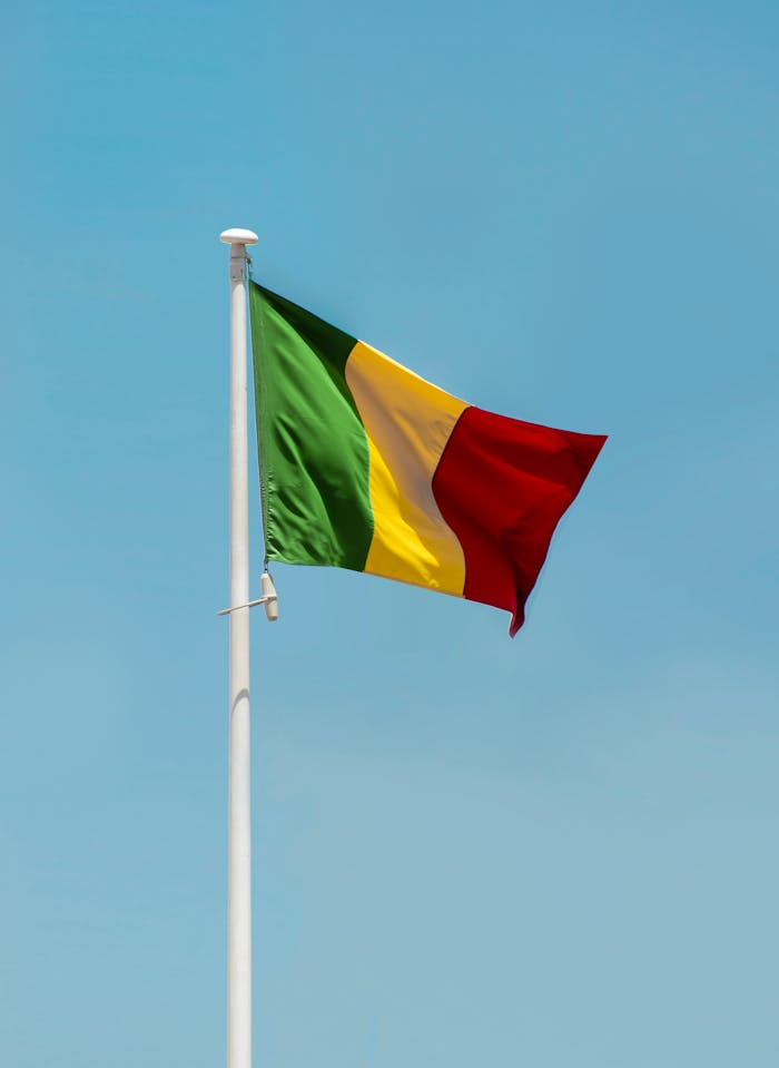 Mali national flag waving on a flagpole against a clear blue sky in Bamako.